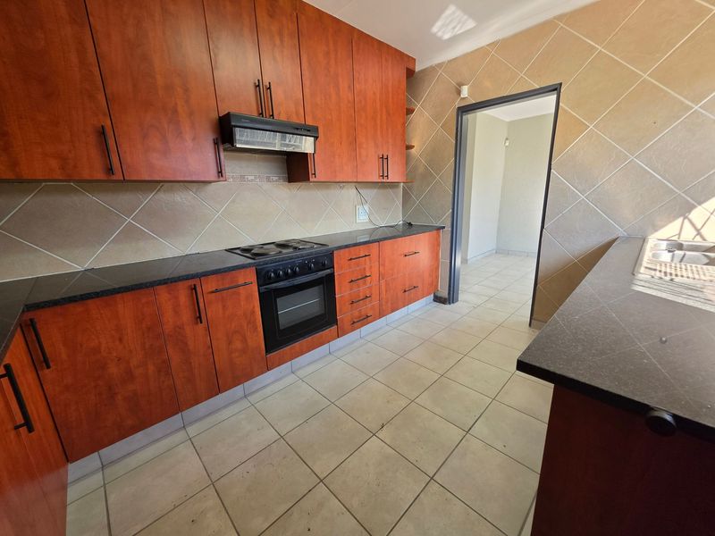 A functional kitchen featuring warm-toned wooden cabinetry, dark granite countertops, built-in oven and hob, and neutral tiled flooring throughout.