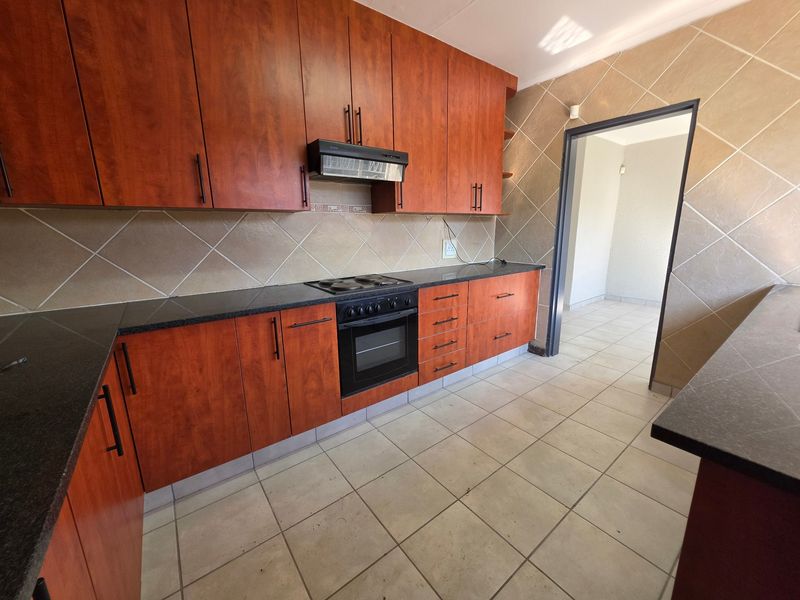A functional kitchen featuring wood-finish cabinetry, granite countertops, and built-in cooking appliances with a tiled backsplash and floor.