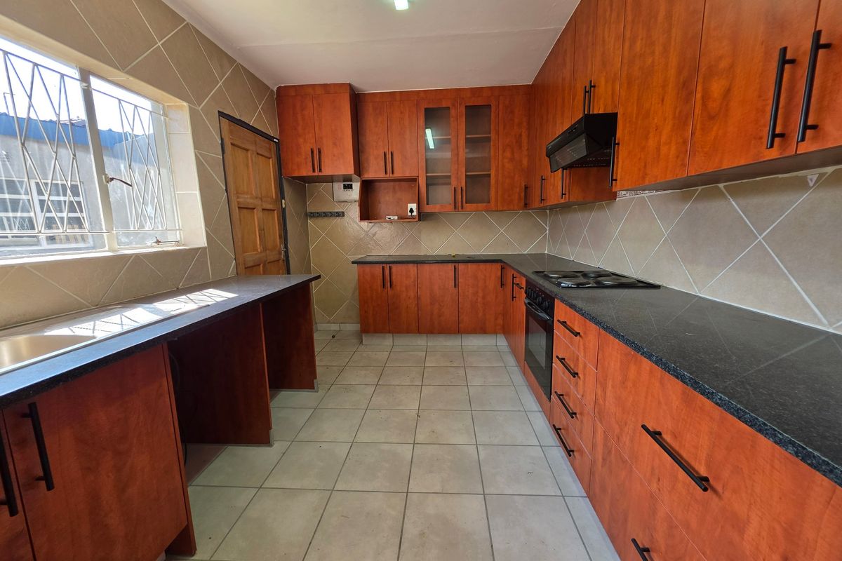 A functional kitchen featuring wood-look cabinetry, dark countertops, built-in oven and hob, and tiled finishes throughout.