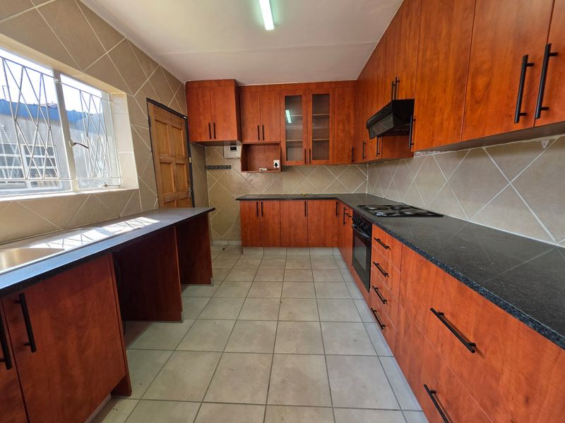 A functional kitchen featuring wood-look cabinetry, dark countertops, built-in oven and hob, and tiled finishes throughout.