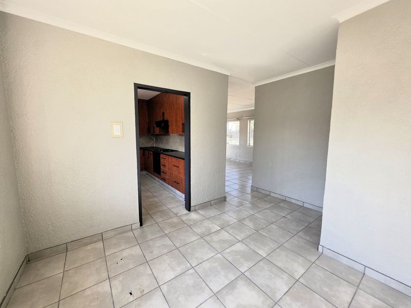 An open-plan living area featuring neutral tiled flooring and a view into a separate kitchen space with built-in cabinetry and appliances.