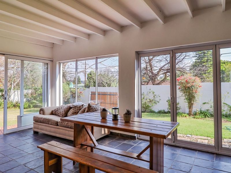 Bright enclosed patio featuring exposed beam ceilings, tiled flooring, and large glass doors providing seamless access to the garden.