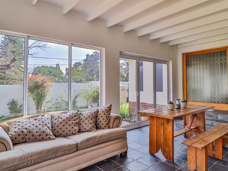 A bright, enclosed patio featuring slate tile flooring, exposed beam ceilings, and large windows providing views of the garden.