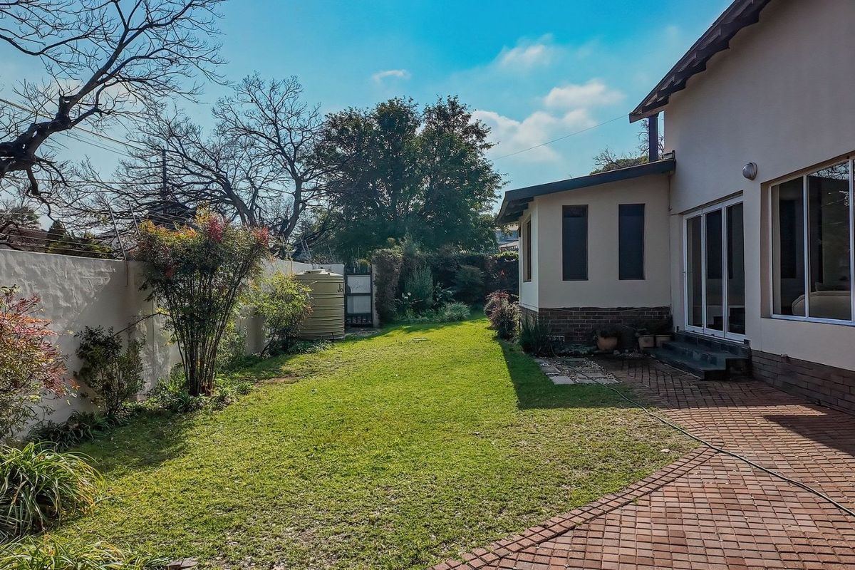 A private rear garden featuring a paved patio area, well-maintained lawn, boundary wall with electric fencing, and a water storage tank.