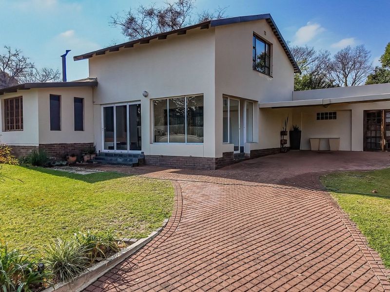 Front view of a two-story residential house featuring a brick paved driveway, covered carport, and established garden surroundings.