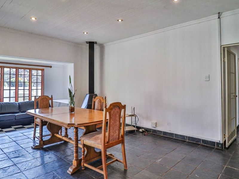 Spacious dining area featuring slate tile flooring, a central freestanding fireplace, and recessed lighting, with an adjacent living space visible.