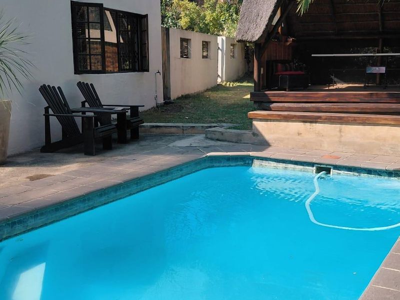 Outdoor pool area featuring a swimming pool with paved surround and a covered thatched lapa with timber decking.