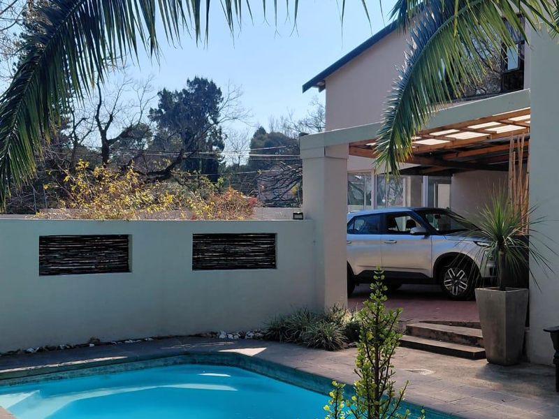 A well-maintained outdoor pool area featuring a paved deck, covered patio space, and a solid boundary wall, perfect for outdoor relaxation.