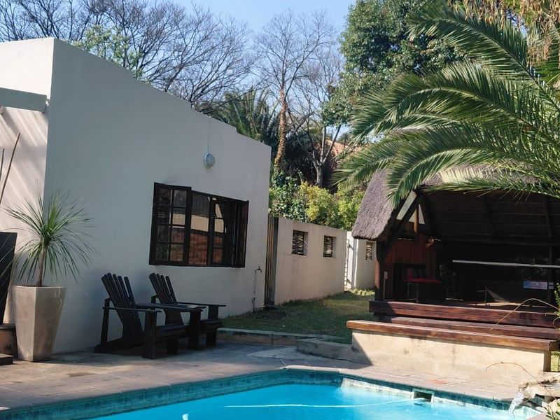 Outdoor pool area featuring a swimming pool, paved surround, timber decking, and a thatched lapa, set within a private garden space.
