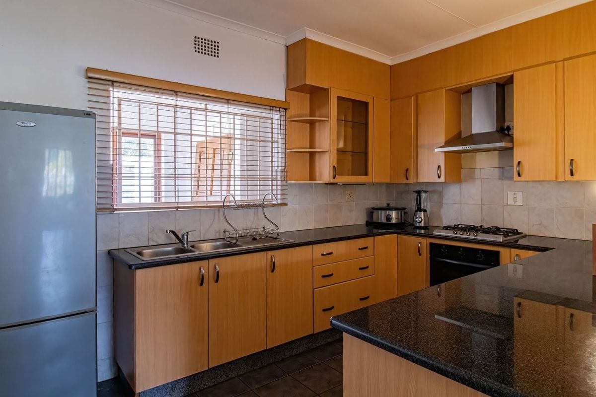 Functional kitchen featuring light wood-tone cabinetry, dark granite countertops, a gas hob with extractor fan, and tiled backsplash.