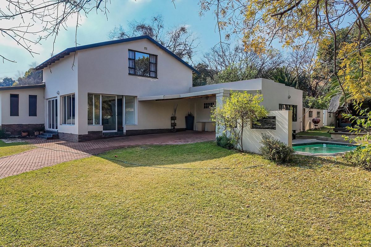 Rear view of the property featuring a paved driveway, covered patio area, and a swimming pool set within a landscaped garden.