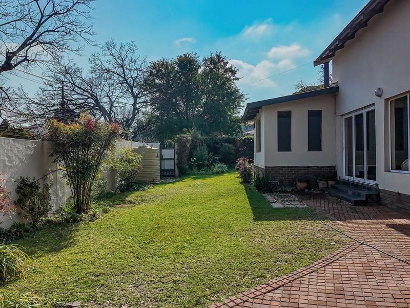 A private rear garden featuring a paved patio area, well-maintained lawn, boundary wall with electric fencing, and a water storage tank.