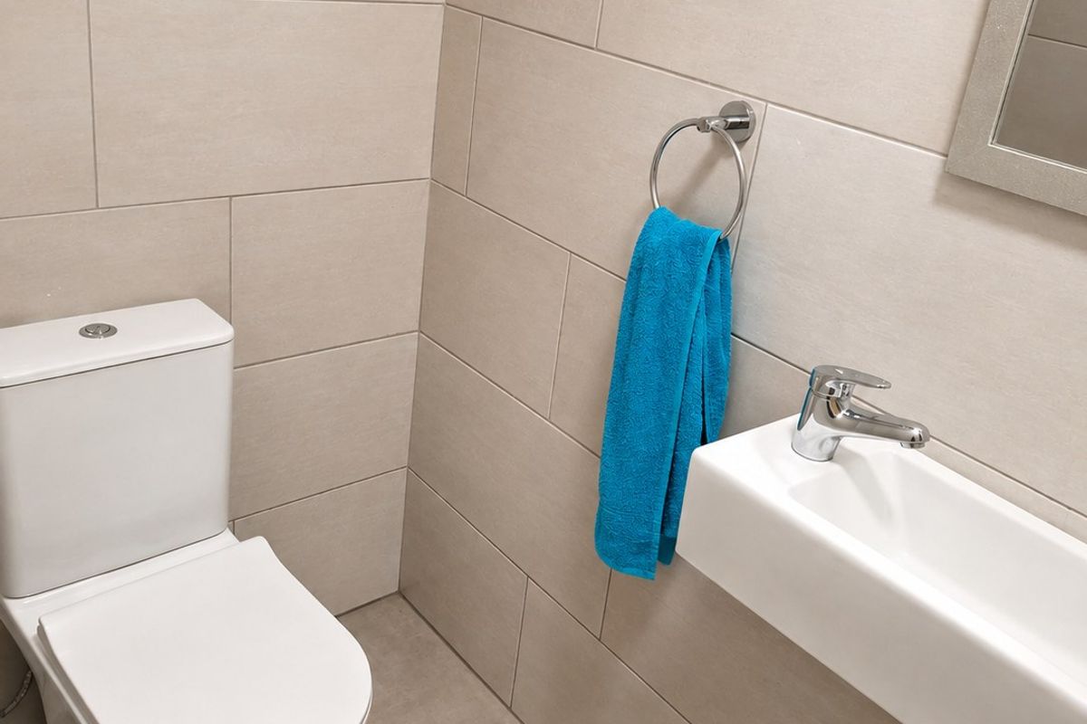 A modern, compact guest bathroom featuring neutral ceramic wall and floor tiles, a wall-mounted basin, and a dual-flush toilet.