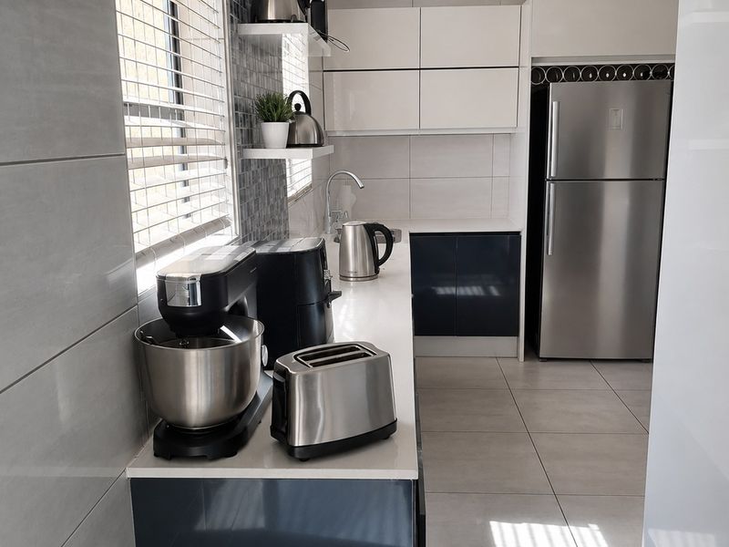 Modern kitchen featuring sleek two-tone cabinetry, stone countertops, tiled backsplash, and high-quality floor tiles with recessed lighting.
