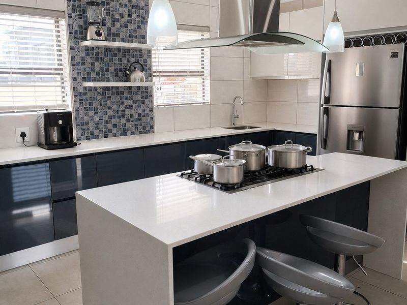 Modern kitchen featuring a central island with a gas cooktop, sleek glossy cabinetry, quartz countertops, and a stylish mosaic tile backsplash.