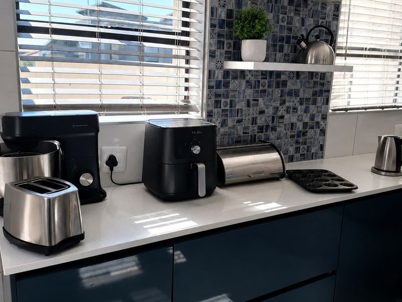 Modern kitchen featuring dark blue handleless cabinetry, white quartz countertops, and a decorative blue mosaic tile backsplash with floating shelving.