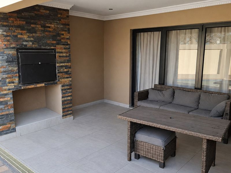 Covered patio featuring a built-in braai with stone cladding, tiled flooring, and direct access to the interior through large sliding glass doors.