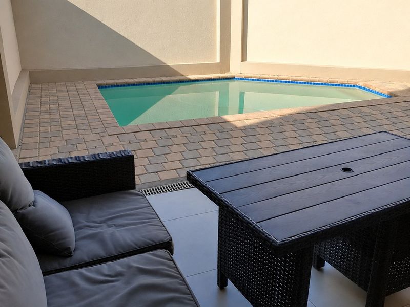 A private outdoor pool area featuring a paved surround, tiled patio space, and high perimeter boundary walls for privacy.