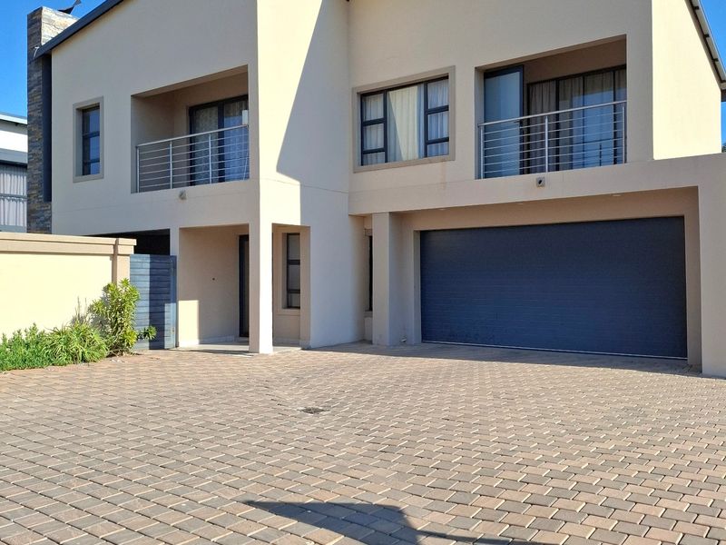 Modern double-story residential property featuring a paved driveway, double garage, and upper-level balconies with metal railings.