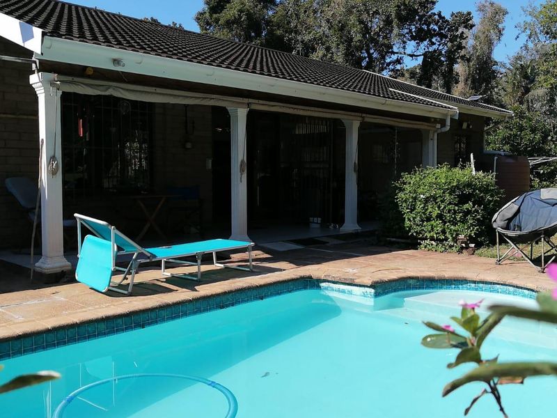 Outdoor pool area featuring a swimming pool with tiled coping, adjacent to a covered patio with decorative columns and brick exterior walls.
