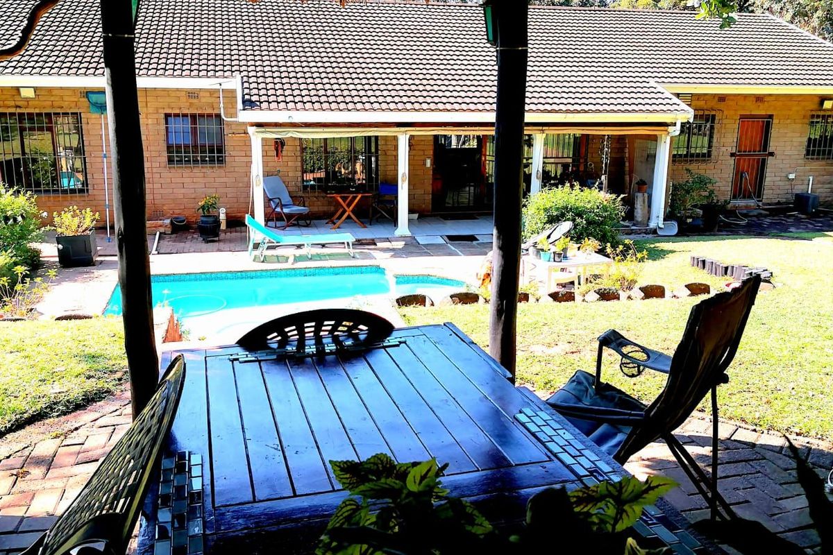 Rear view of the property featuring a covered patio, swimming pool, and established garden area with brick paving.