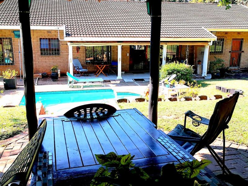 Rear view of the property featuring a covered patio, swimming pool, and established garden area with brick paving.