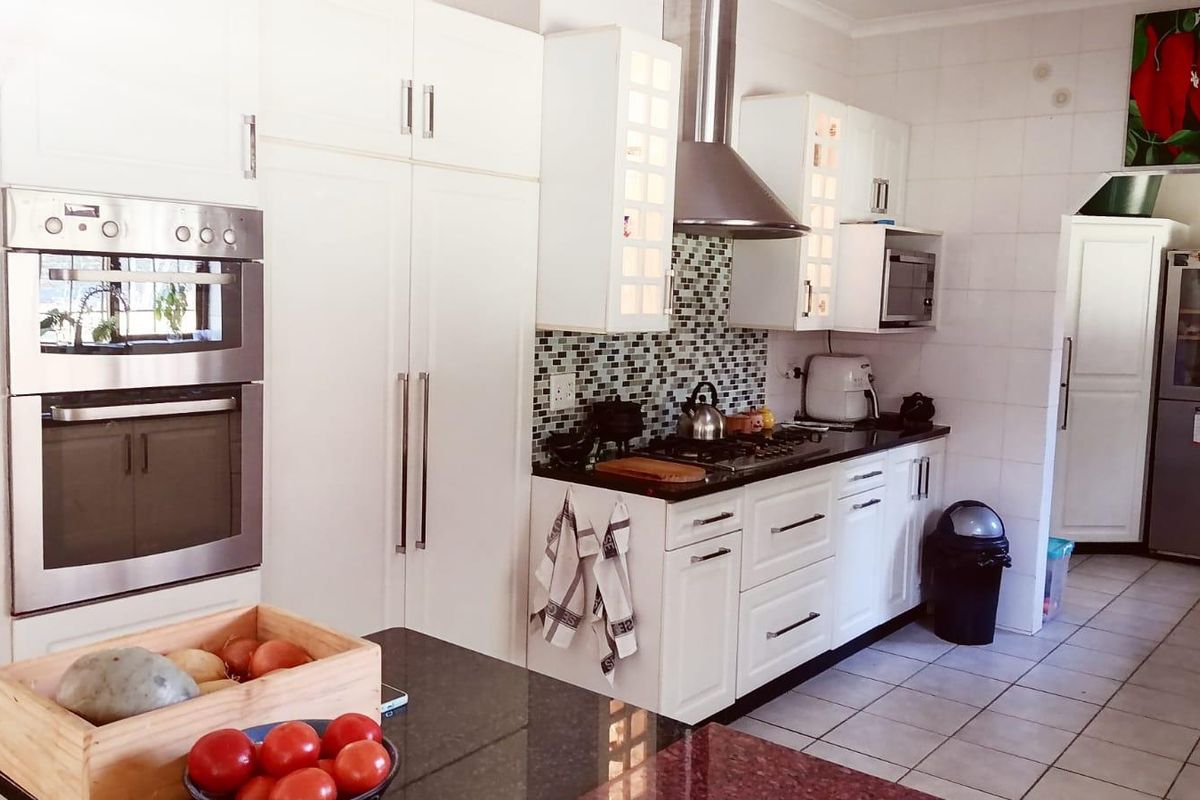 A functional kitchen featuring white cabinetry, granite countertops, a mosaic tile backsplash, and built-in stainless steel appliances including a double oven and extractor fan.