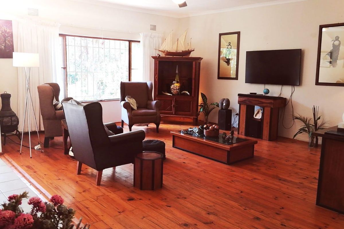 A spacious living room featuring warm timber flooring, a large window with security bars, and a ceiling fan.