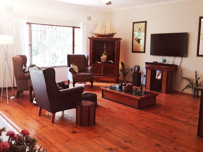 A spacious living room featuring warm timber flooring, a large window with security bars, and a ceiling fan.