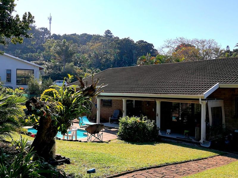 Rear view of the house featuring a covered patio, swimming pool, and a well-maintained garden area with brick facade and tiled roof.