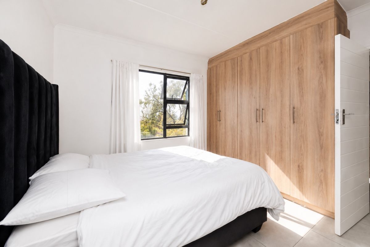 A bright bedroom featuring built-in wooden cupboards, tiled flooring, and a large window with natural light.