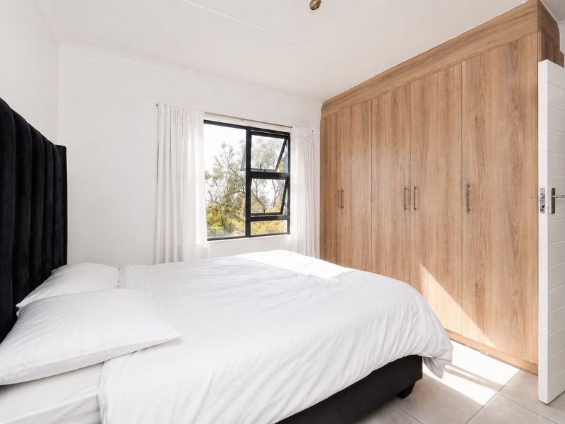 A bright bedroom featuring built-in wooden cupboards, tiled flooring, and a large window with natural light.