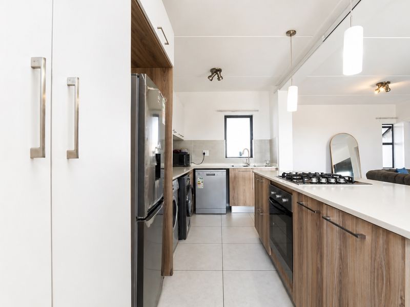 Modern kitchen featuring wood-grain cabinetry, stone countertops, a gas hob, built-in oven, and integrated appliance spaces, flowing into an open-plan living area.