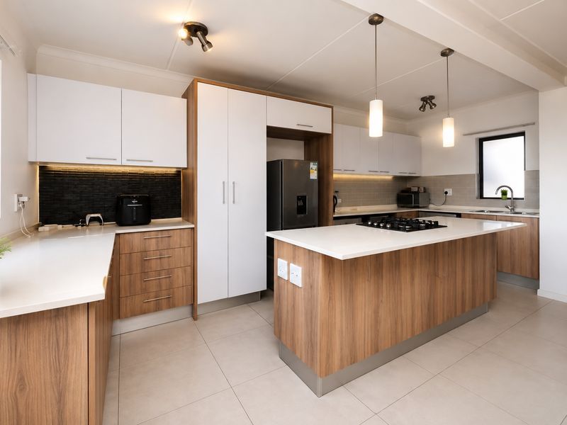 Modern kitchen featuring a central island with gas hob, sleek wood-tone and white cabinetry, stone countertops, and contemporary pendant lighting.