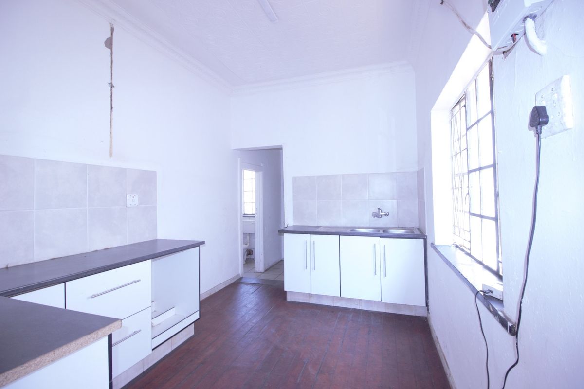 A vacant kitchen featuring built-in cabinetry, laminate countertops, a stainless steel sink, and timber flooring, requiring cosmetic updates and repairs.