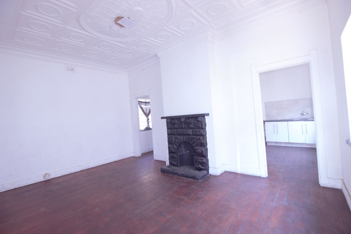 Spacious living room featuring a classic pressed metal ceiling with an ornate rose, a stone fireplace, and original timber flooring.