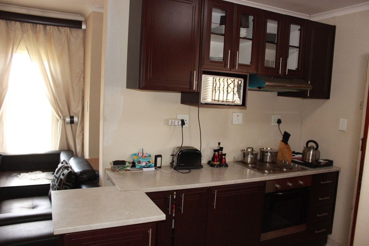 Compact kitchen featuring dark wood cabinetry, laminate countertops, and integrated appliances, with adjacent living area visible.