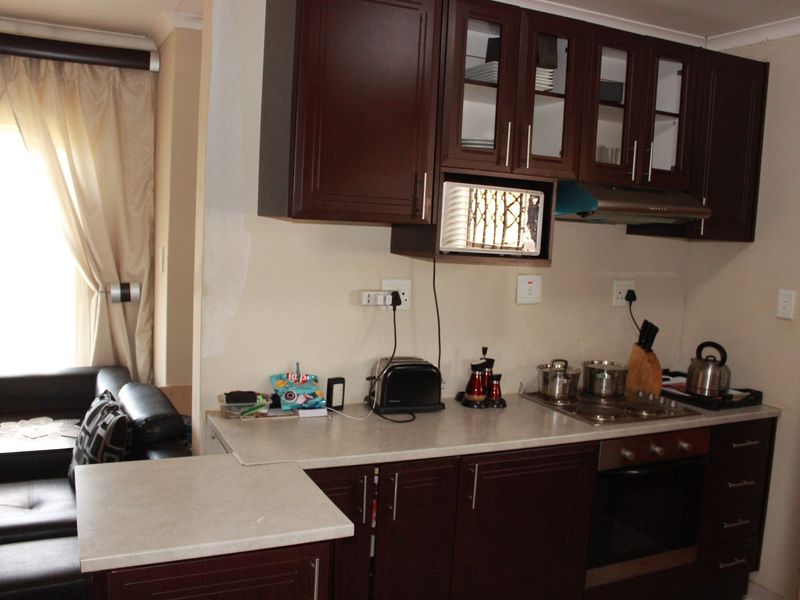 Compact kitchen featuring dark wood cabinetry, laminate countertops, and integrated appliances, with adjacent living area visible.