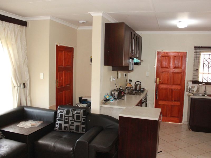 Open-plan living and kitchen area featuring dark wood cabinetry, laminate countertops, tiled flooring, and direct access to internal doors.