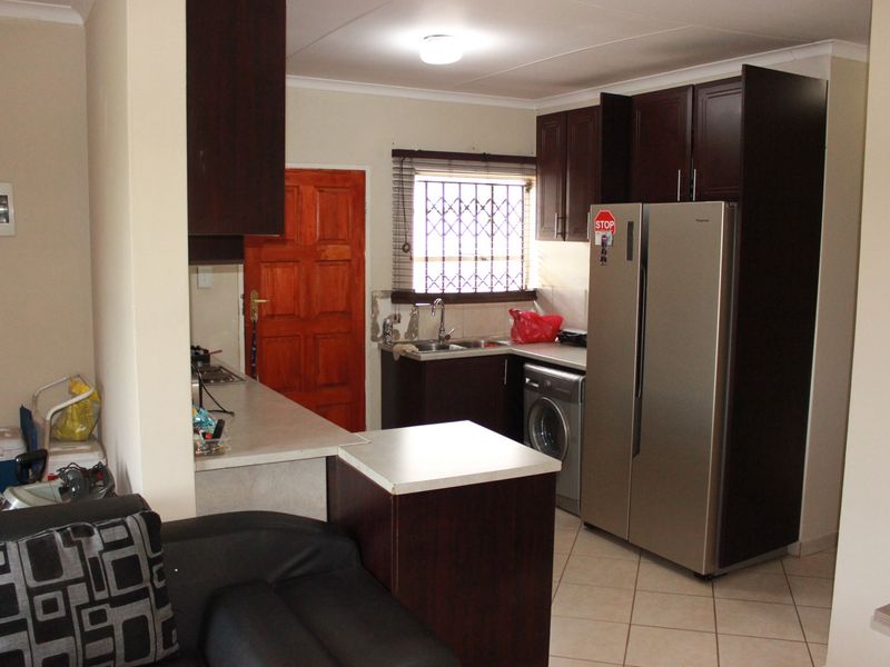 A functional kitchen featuring dark wood cabinetry, laminate countertops, tiled flooring, and a window with security bars, providing a practical workspace.