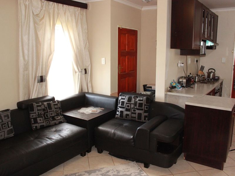 Open-plan living area featuring tiled flooring and a compact kitchen with dark wood cabinetry and laminate countertops.