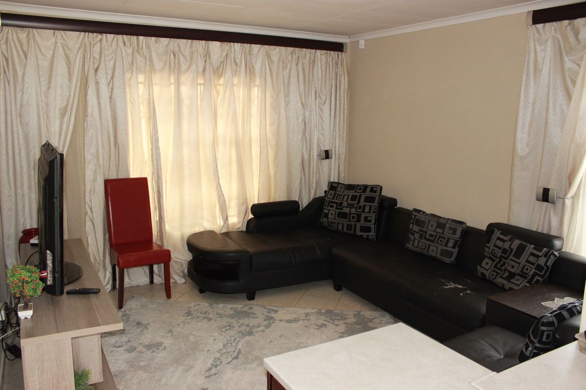 A living room area featuring tiled flooring and full-length window curtains.
