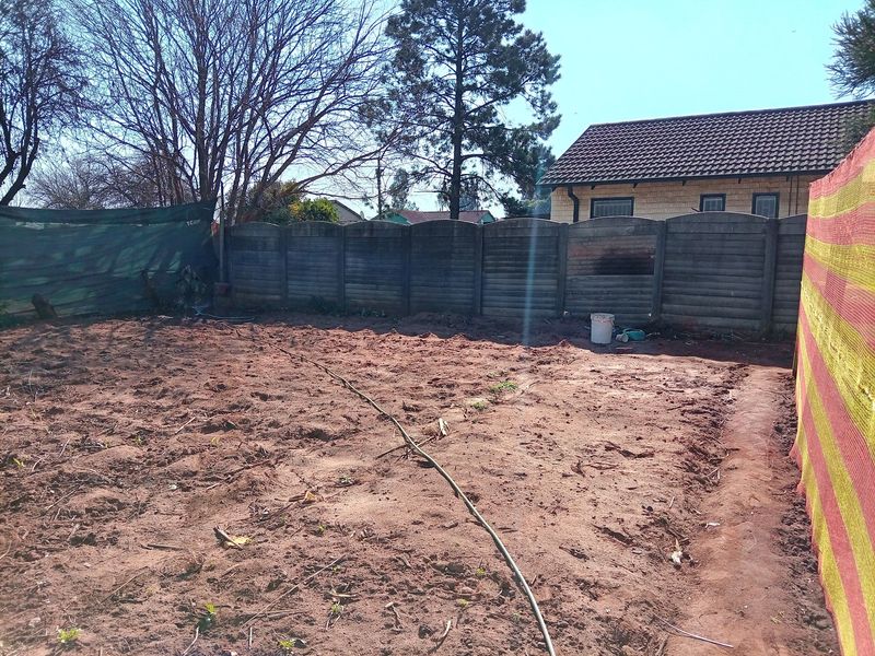A large, unlandscaped backyard area featuring a precast concrete boundary wall and views of the main house structure.