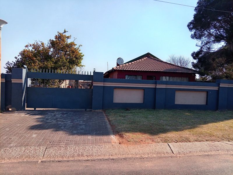 Front view of a residential property featuring a paved driveway, secure perimeter wall with sliding gate, and a tiled roof structure.