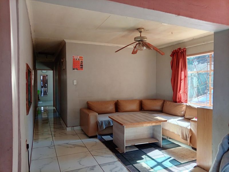 A living room featuring tiled flooring, a ceiling fan, and security bars on the window, showing signs of wear on the ceiling.