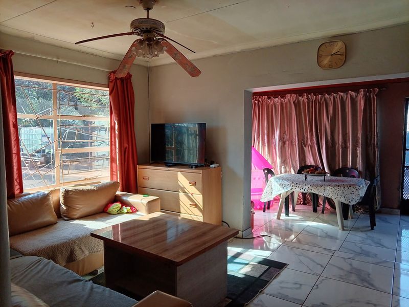 Open-plan living and dining area featuring tiled flooring, a ceiling fan, and large windows with security bars, offering a functional layout for daily living.