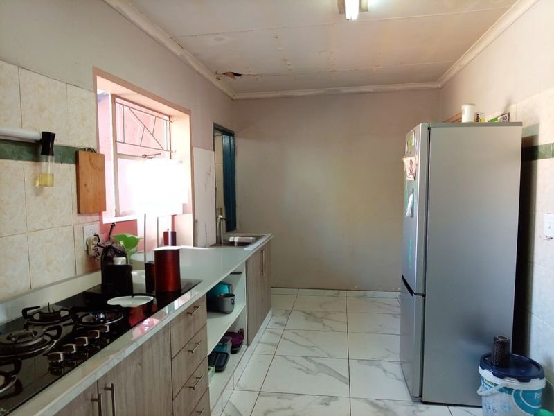 A functional kitchen featuring built-in cabinetry, a gas hob, and tiled flooring, requiring ceiling repairs and cosmetic updates to improve its overall condition.