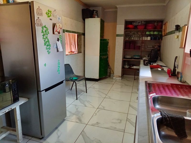 A functional kitchen featuring tiled flooring, a double bowl stainless steel sink, and open built-in shelving with tiled splashback finishes.