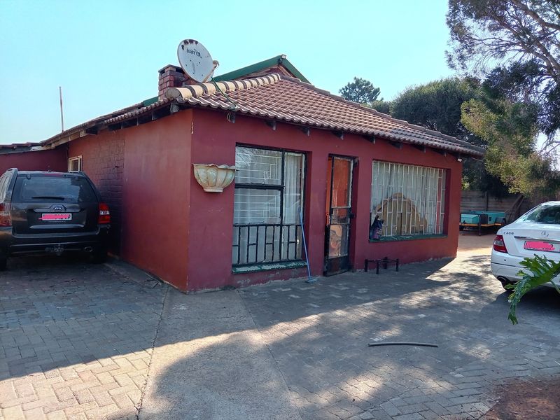 Front exterior view of a single-story brick house featuring a tiled roof, paved driveway, and security bars on windows.