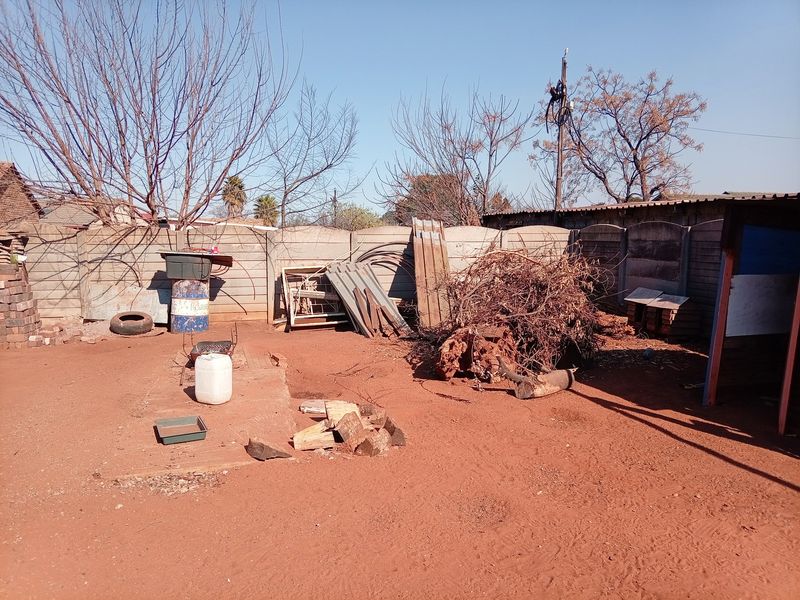 A rear outdoor area featuring a precast concrete boundary wall and an unlandscaped yard space requiring clearing and development.